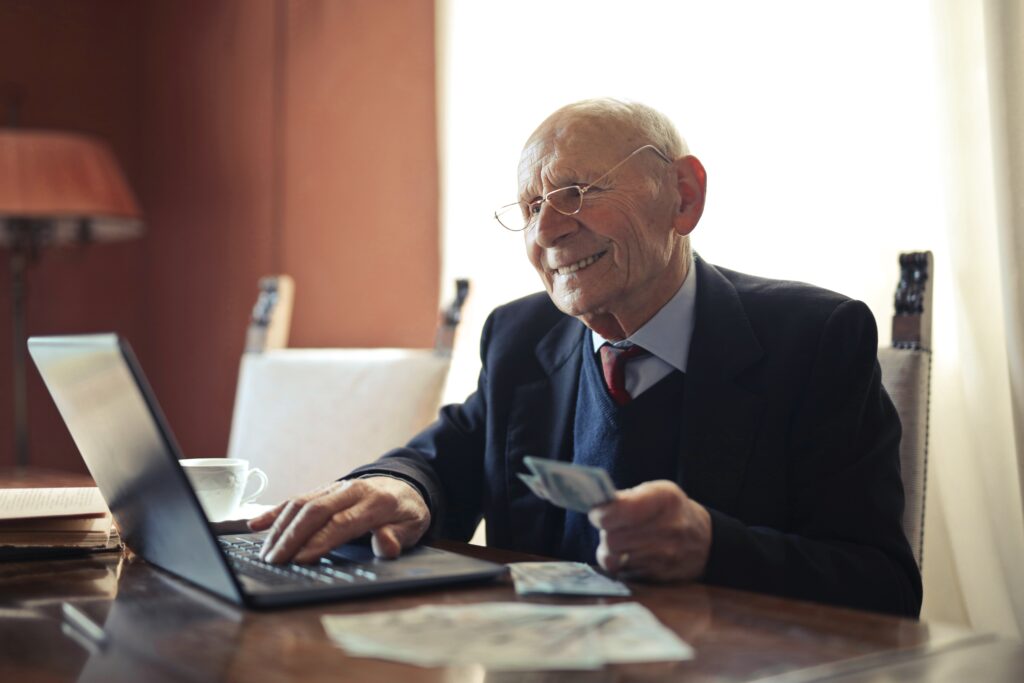 Älterer Herr mit Geld am Laptop